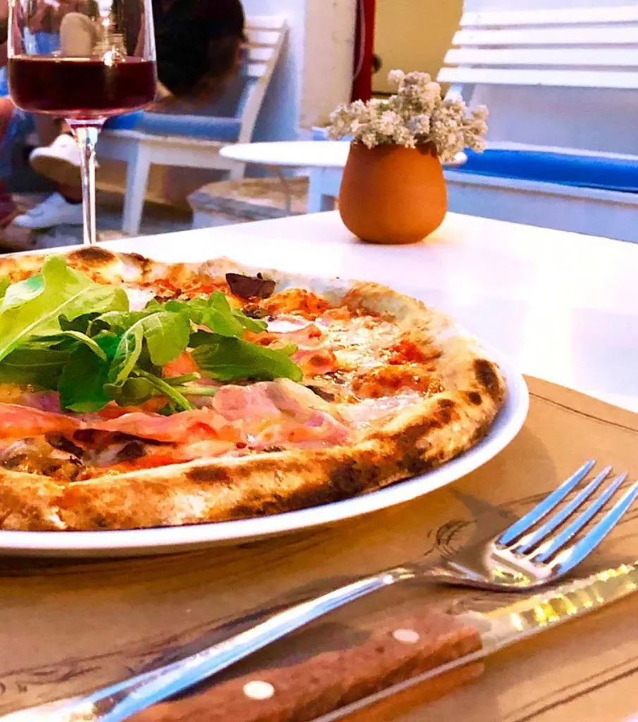 Pizza topped with arugula and cured ham next to a glass of red wine on an outdoor table at 49 Çukurcuma