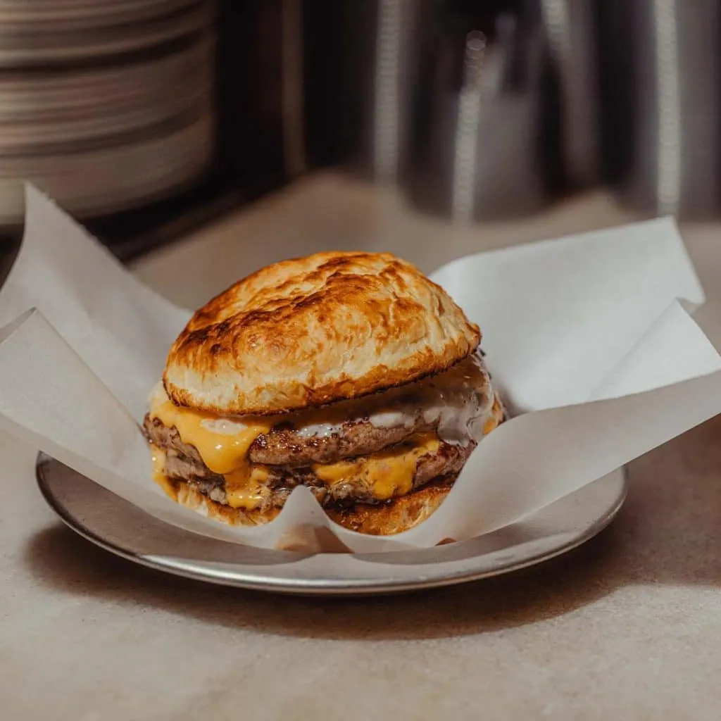 Akali cheeseburger with melted cheddar and house sauce, served in white paper on a small metal tray