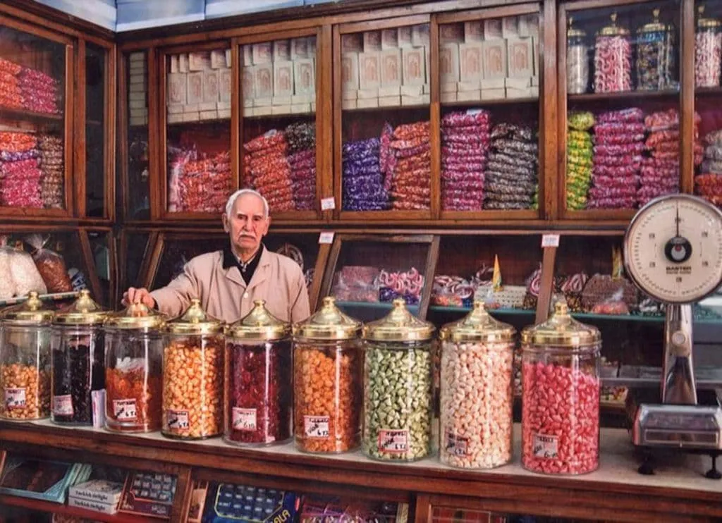 Shopkeeper behind rows of brass-lidded glass jars of akide candy at Altan Şekerleme