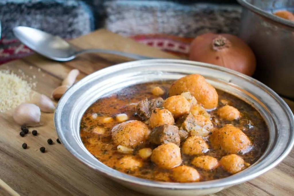 Analı Kızlı soup in a metal bowl, stuffed bulgur balls and chickpeas in a red broth