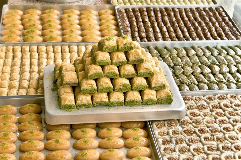 Pyramid of pistachio baklava stacked on a platter between shop trays of şekerpare and walnut baklava