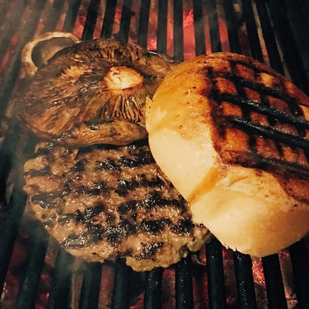 Beef patty, portobello mushroom, and grill-marked bun cooking over glowing charcoal at Biber Burger