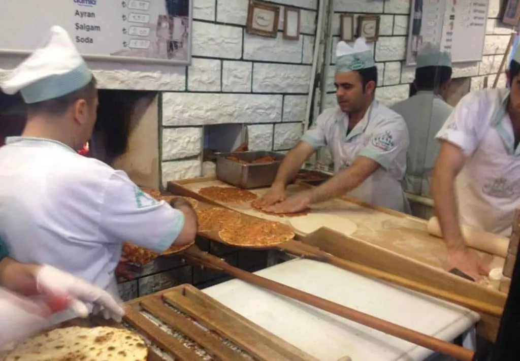 Bakers working lahmacun on long wooden peels in front of the stone oven at Borsam Taşfırın