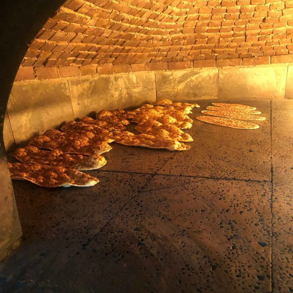 Oval lahmacun baking on the stone floor of a domed brick oven at Buketist