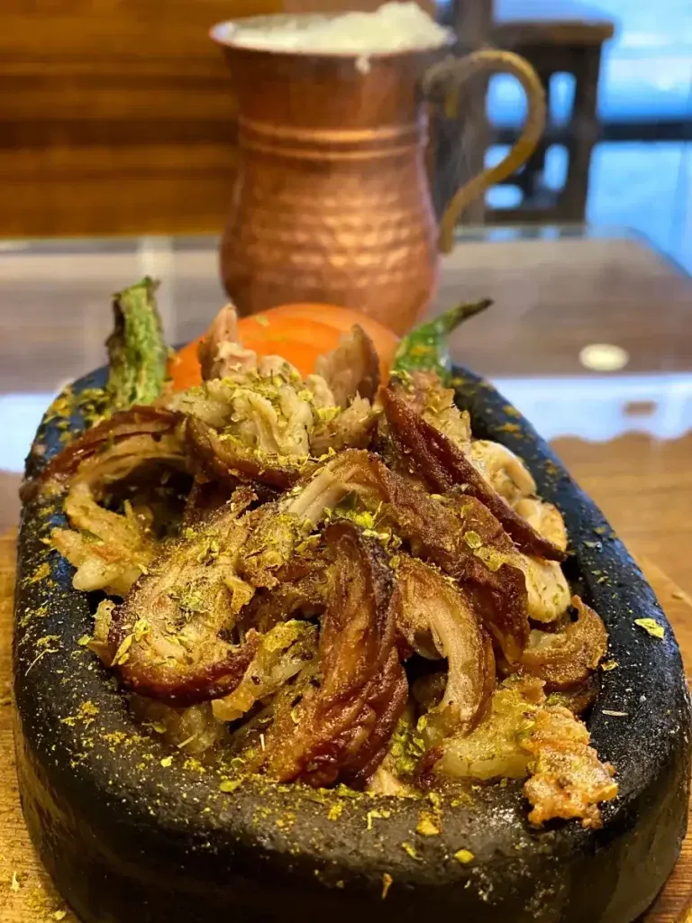 Chopped kokoreç dusted with oregano in a hot stone dish at Gala Kokoreç, with a copper pitcher behind