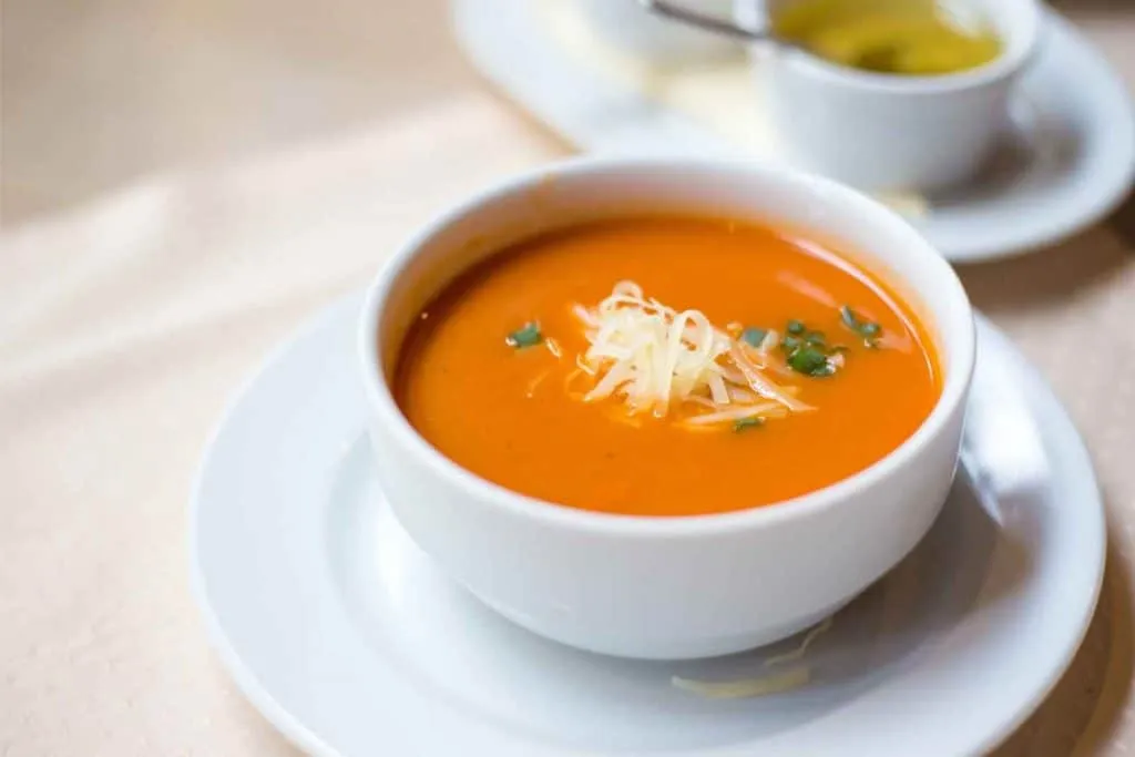 Turkish tomato soup in a bowl served with shredded yellow cheese