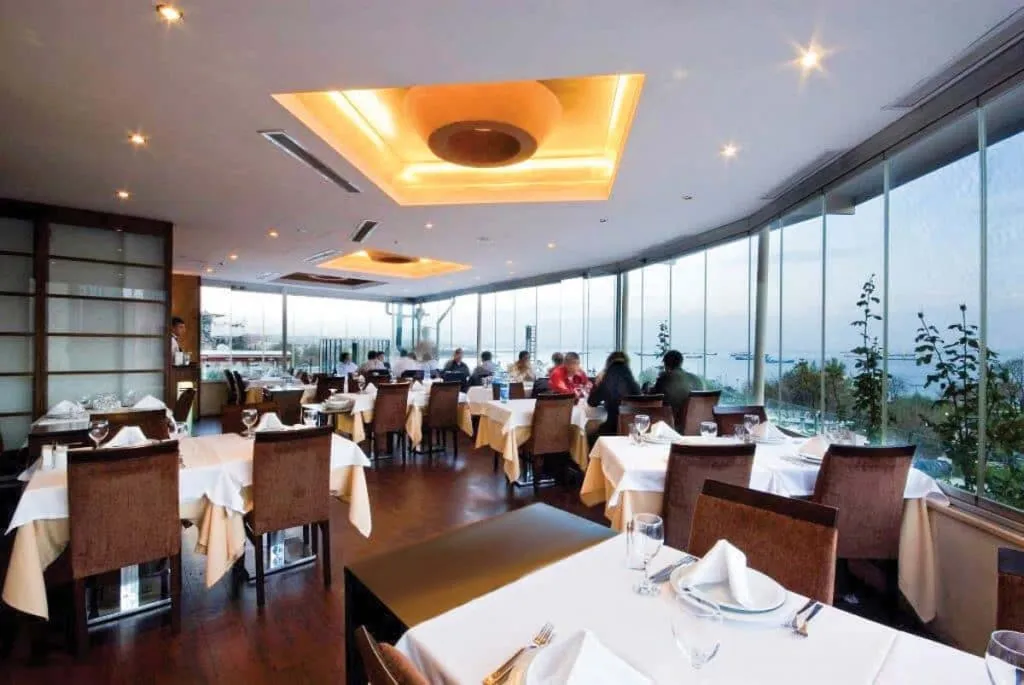 White-tablecloth dining room at Develi Samatya with wraparound windows over the Sea of Marmara