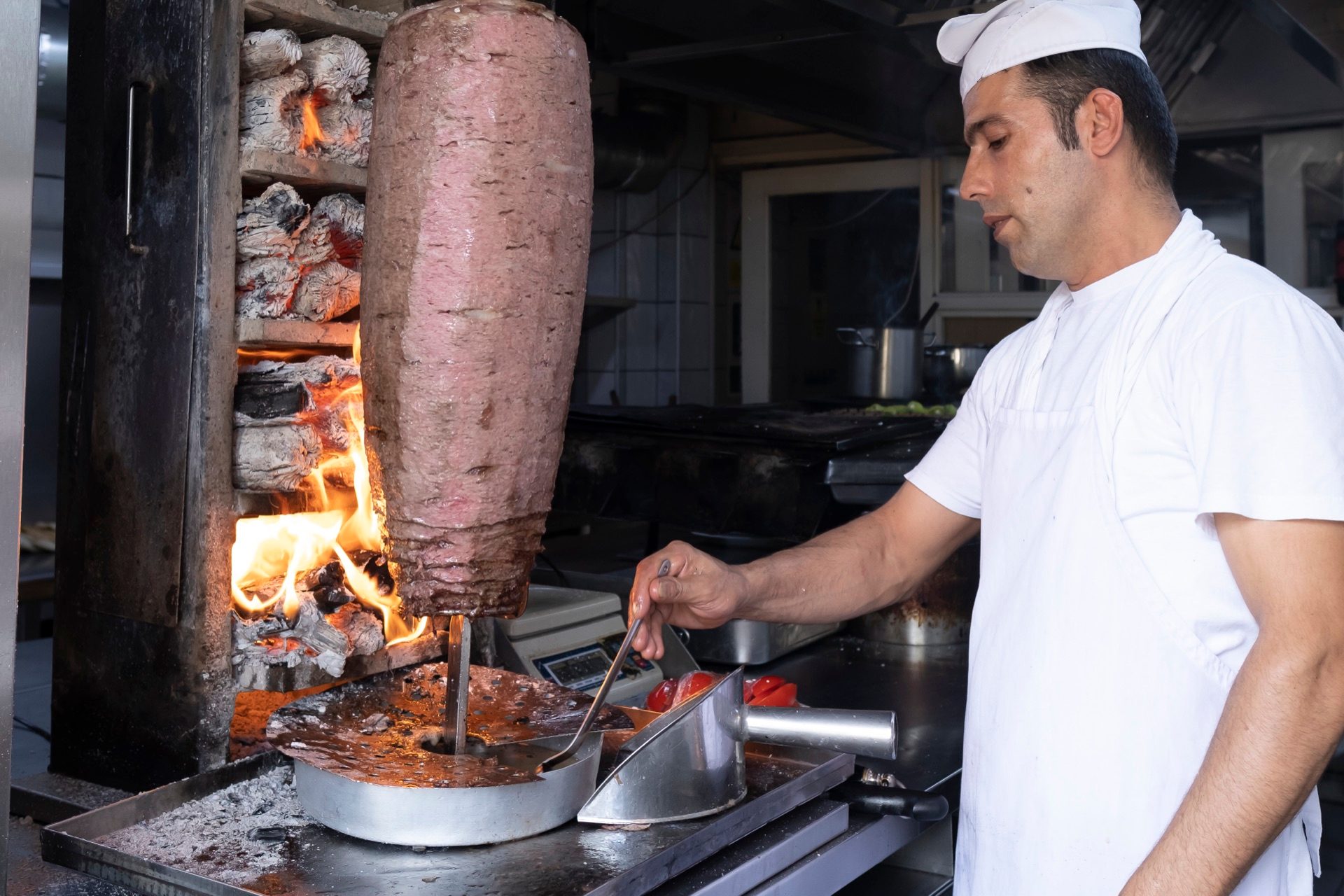 Closeup of a doner kebab over charcoal flames as the chef slices meat with a long knife