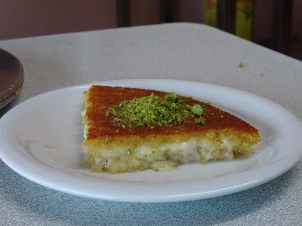 Slice of künefe at Ekol Hatay with ground pistachio on top and melted cheese showing at the cut edge