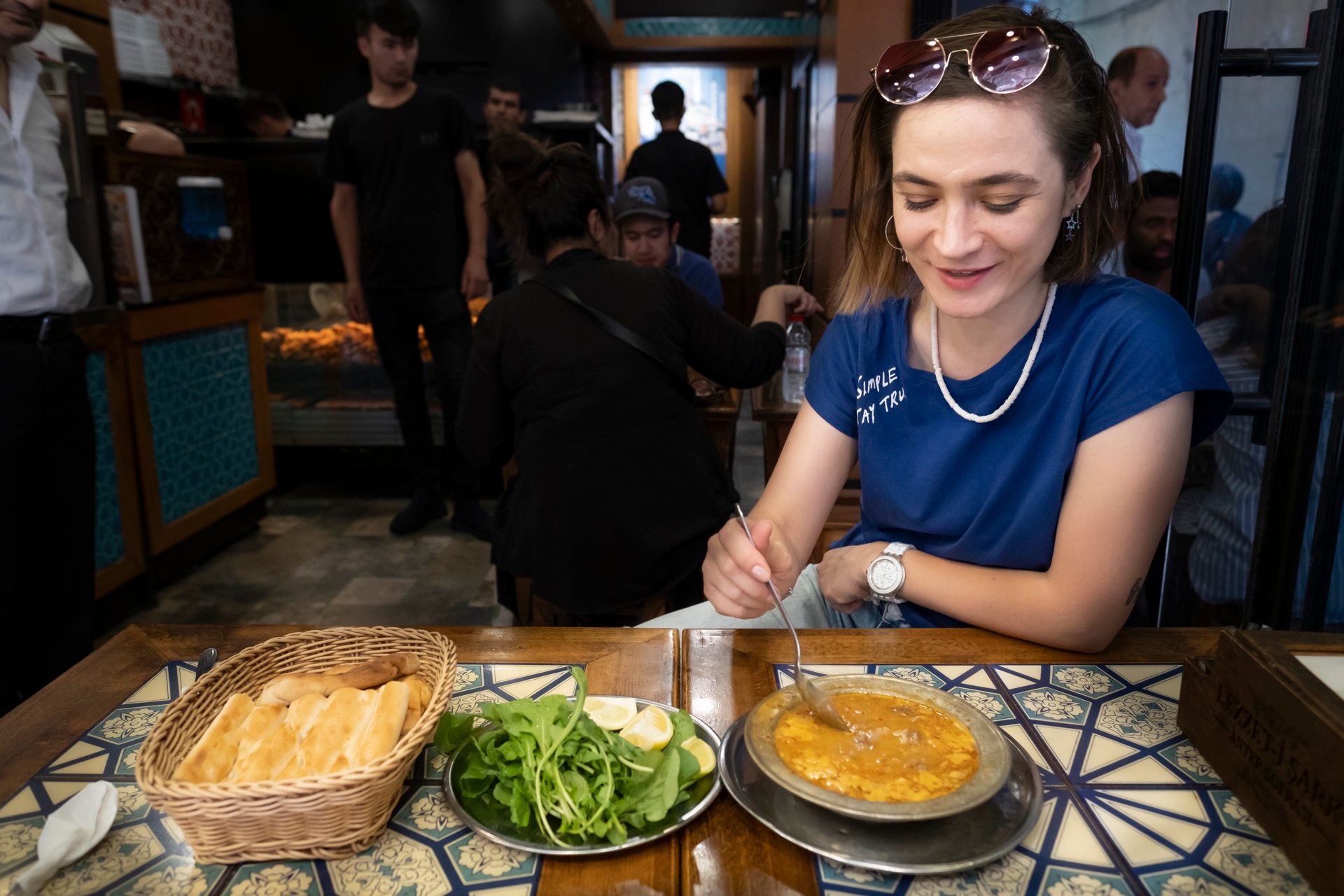 Smiling guest at a traditional Istanbul lokanta table with a metal plate, arugula salad, and a basket of bread