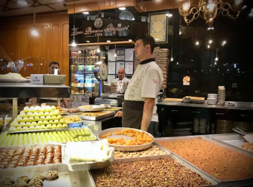 Counter staff at Hacı Bozan Oğulları behind trays of baklava, syrup-soaked sweets, and pistachios