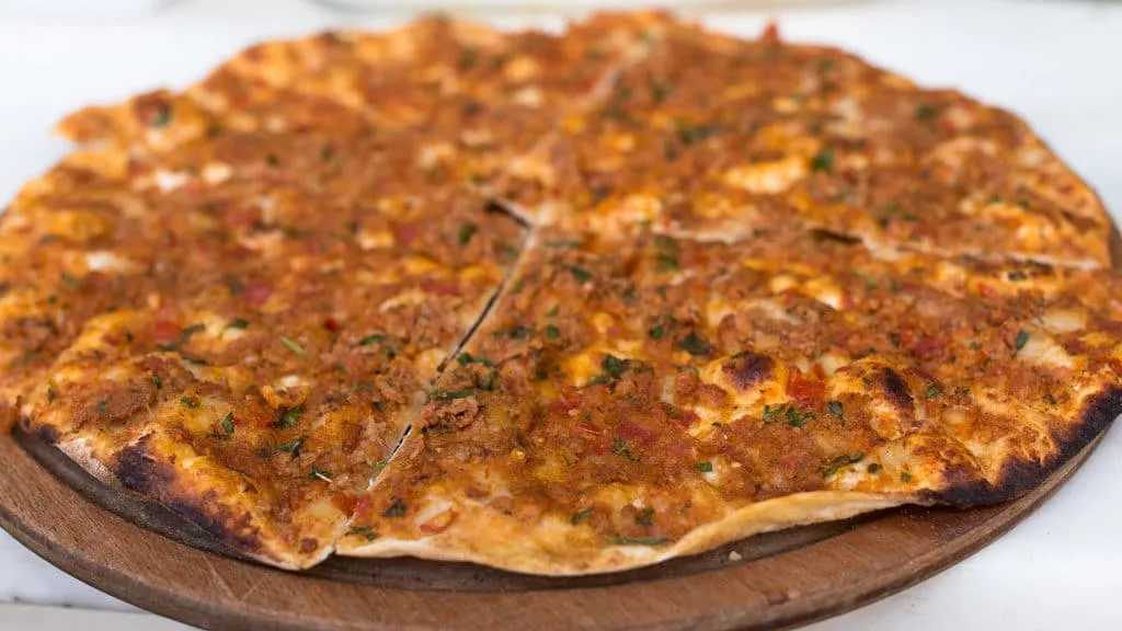 Crispy Turkish lahmacun cut into 4 pieces on a circular wooden tray