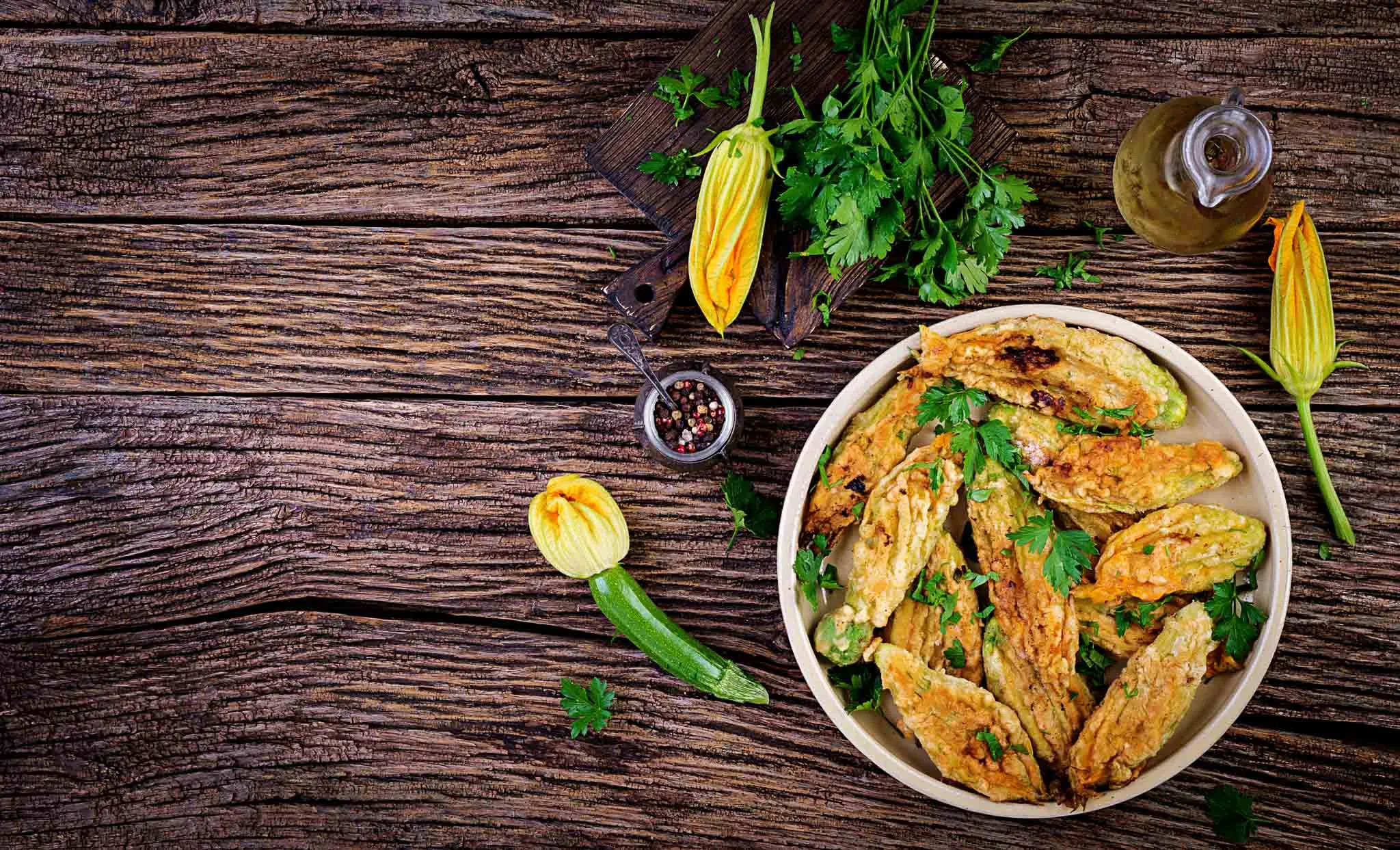 Stuffed zucchini flowers in a bowl on a wooden table with parsley and fresh blossoms