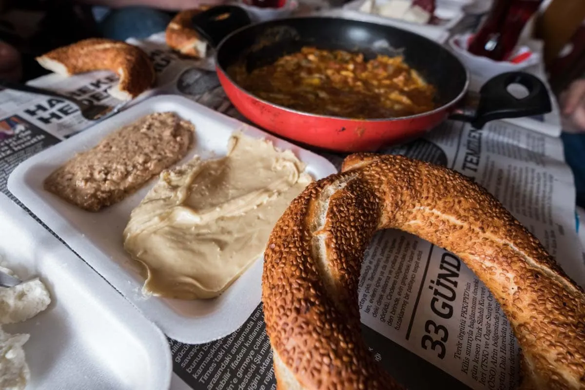 Sesame simit ring beside tahini and nut spreads on a tray over Turkish newspaper