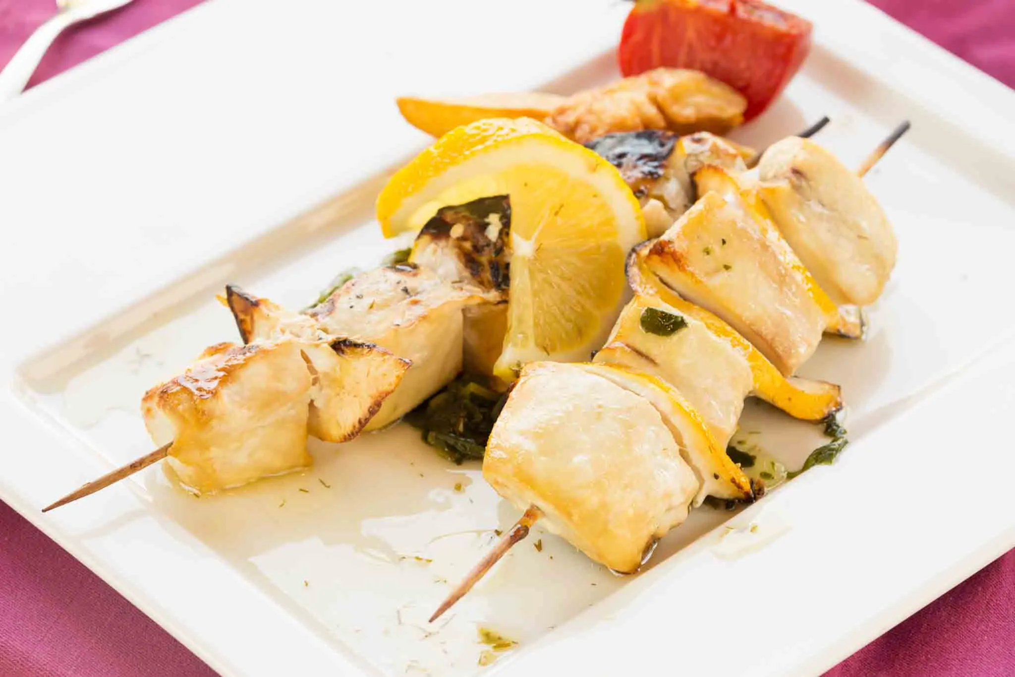 Grilled swordfish skewers with lemon slices and tomato on a white plate