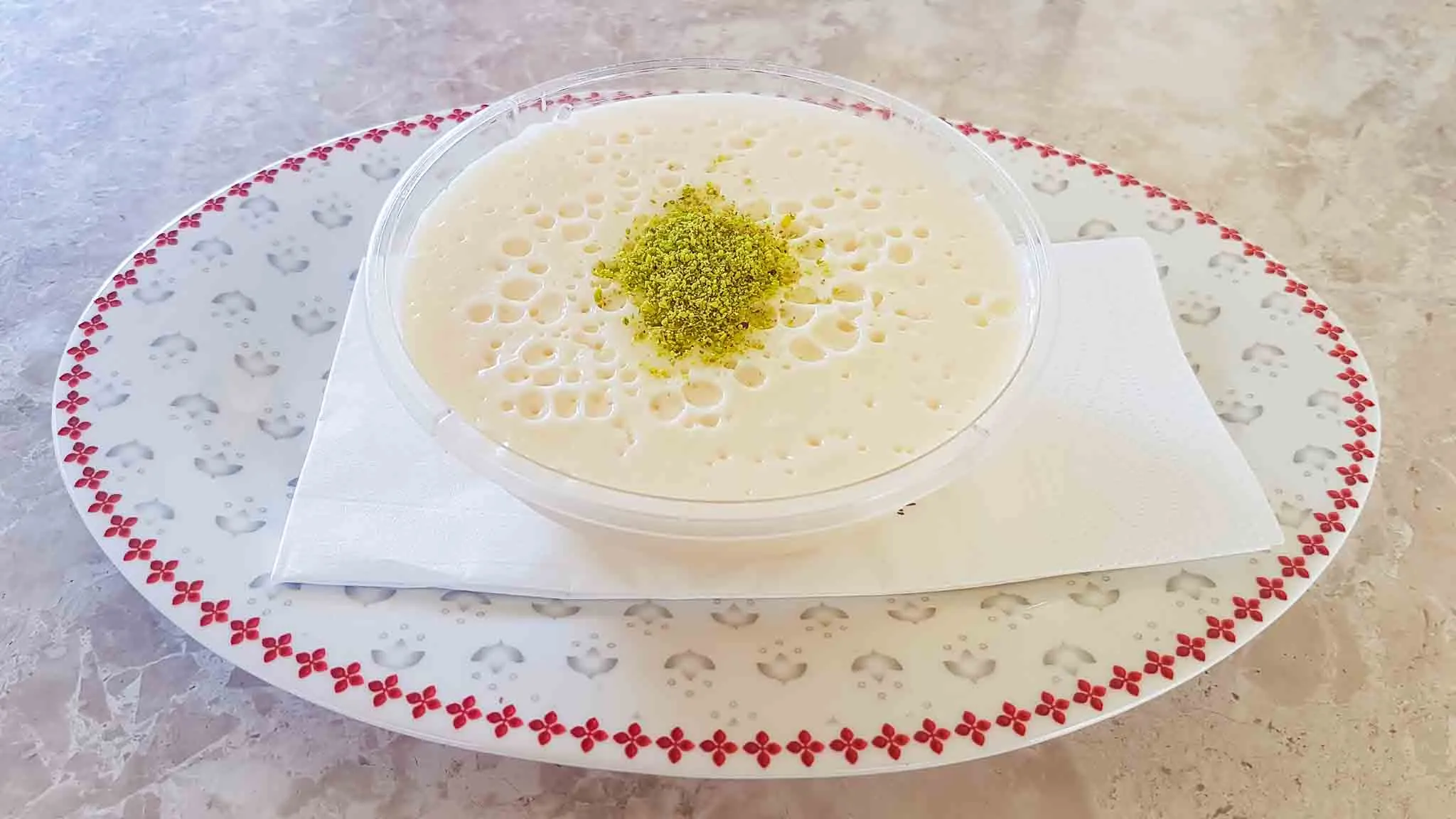 White milk pudding topped with ground pistachio in a clear bowl on a floral-rimmed plate