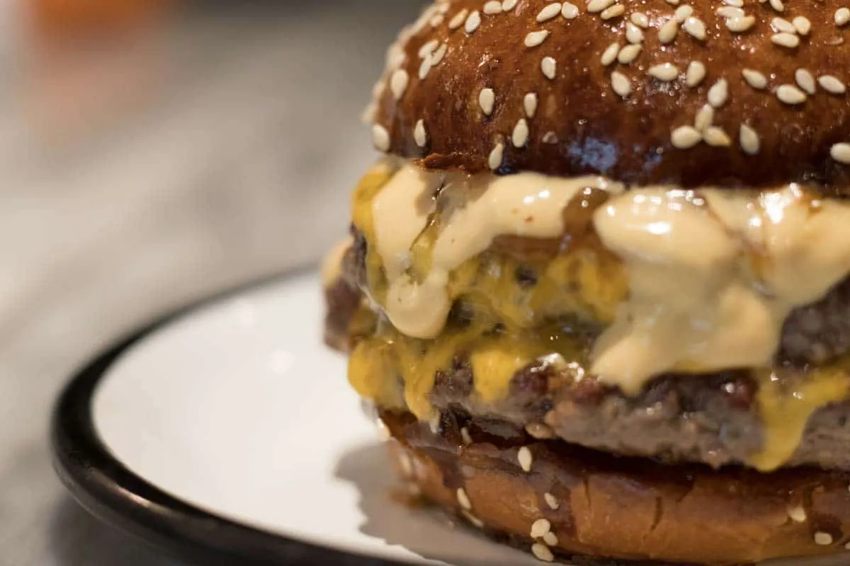 Close-up of a cheeseburger on a toasted sesame bun, melted cheddar and sauce dripping over the patty