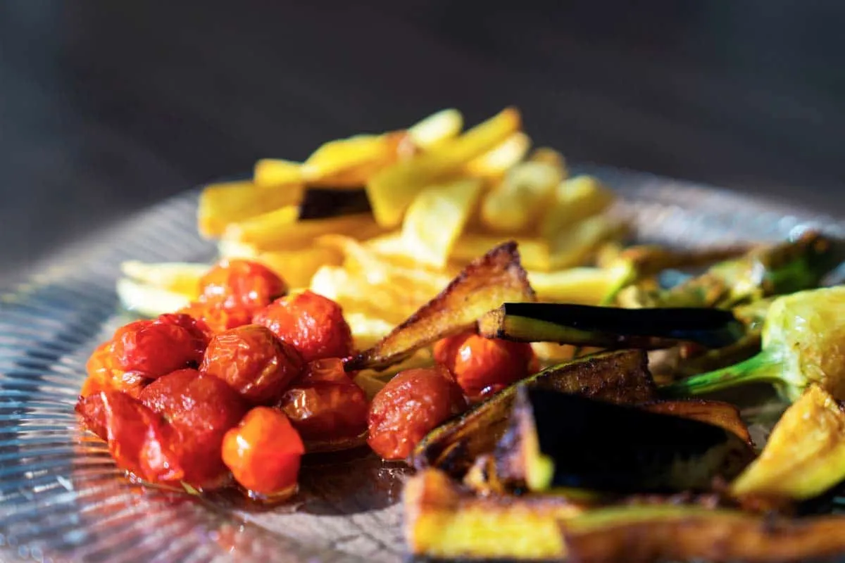 Fried eggplant strips, green peppers, and cherry tomatoes on a glass plate