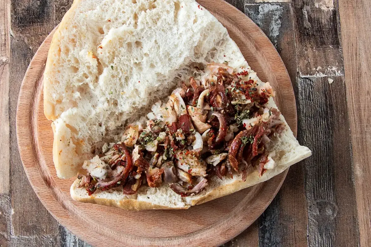 A chopped kokoreç sandwich on crusty bread served on a round wooden board