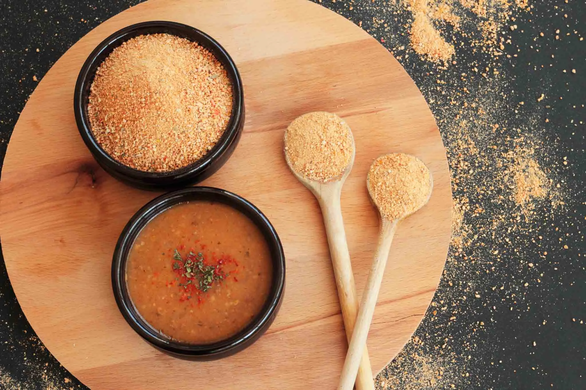 Bowl of cooked tarhana soup beside dried tarhana powder and two wooden spoons on a board