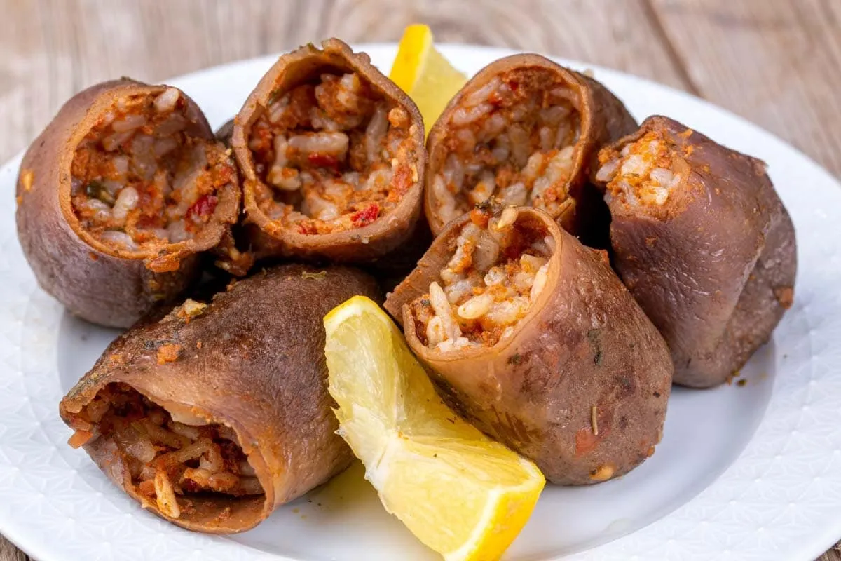 Rice-stuffed dried eggplant rolls on a white plate with lemon wedges