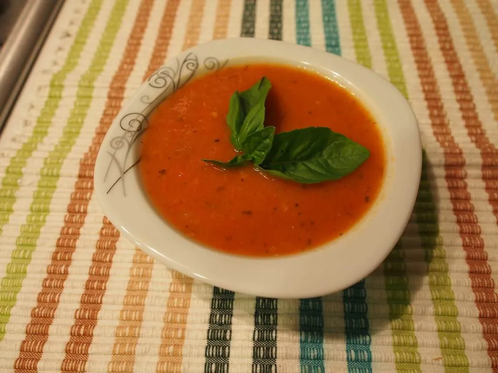 Small bowl of turkish tomato soup topped with fresh basil leaves on striped tablecloth