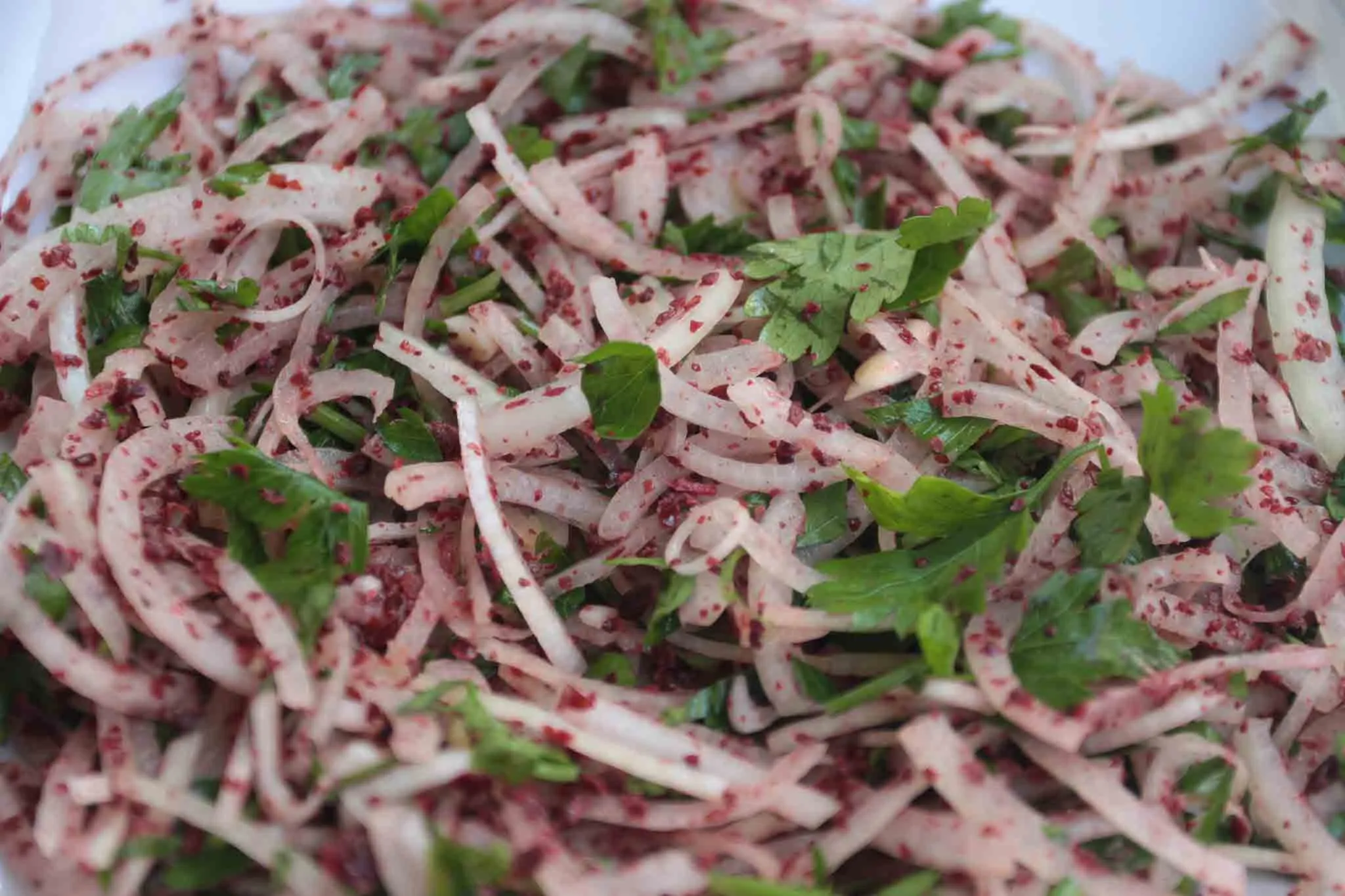 Thin-sliced onions tossed with red sumac and chopped parsley in a white dish