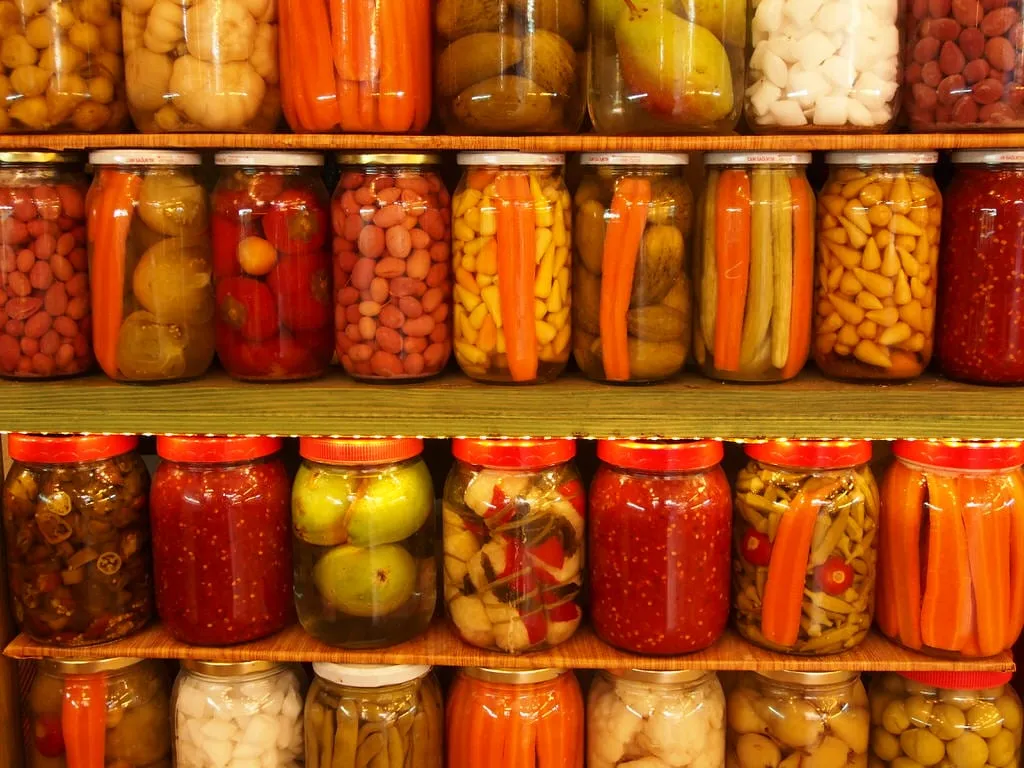 4 shelves filled with jars of colorful pickles including peppers, okra, carrots, garlic, cauliflower and more