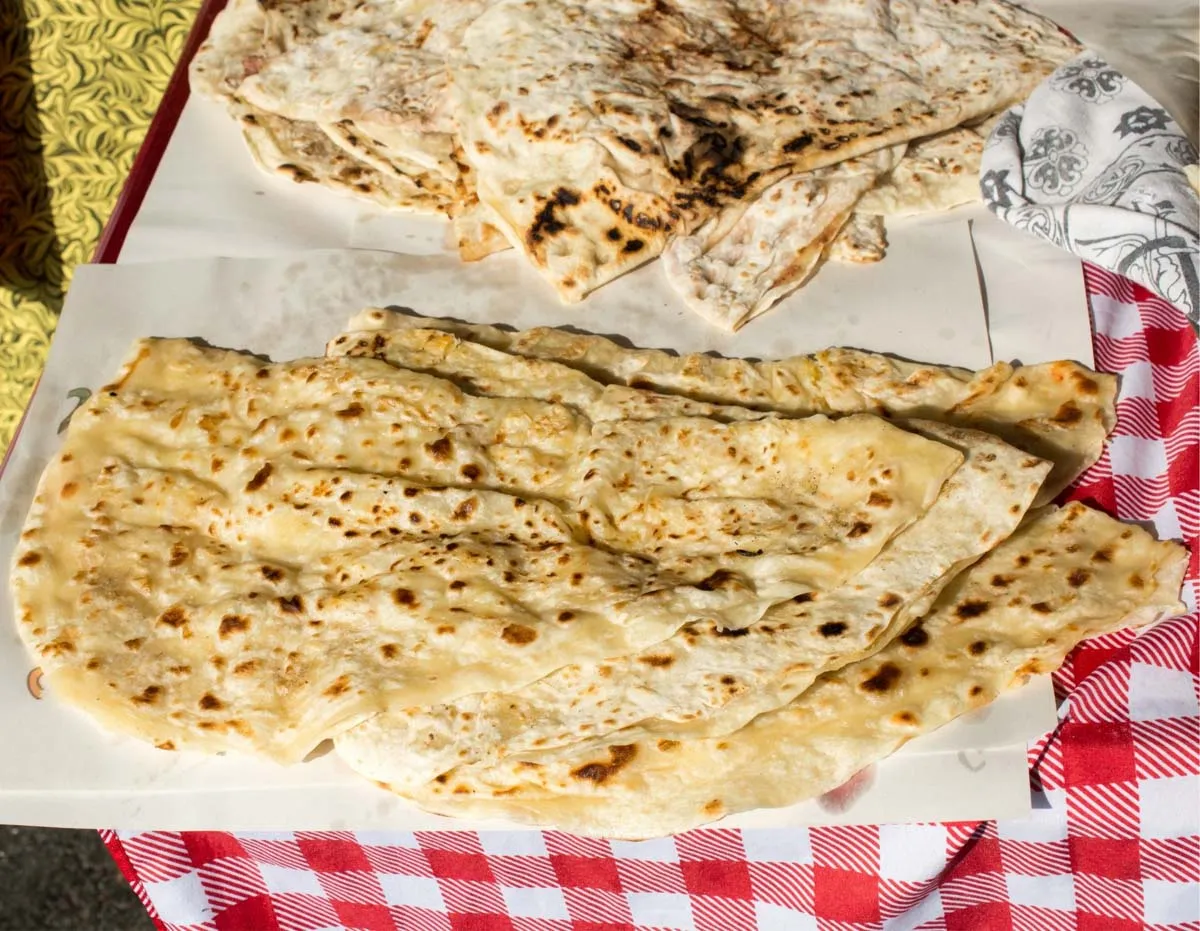 Folded gozleme flatbreads with browned spots on parchment paper over a red checkered tablecloth