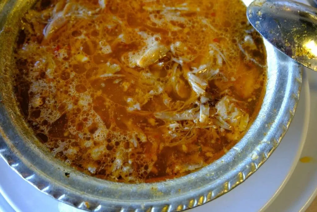 Close-up of kelle paça soup in a hammered metal bowl, shredded meat in a paprika broth