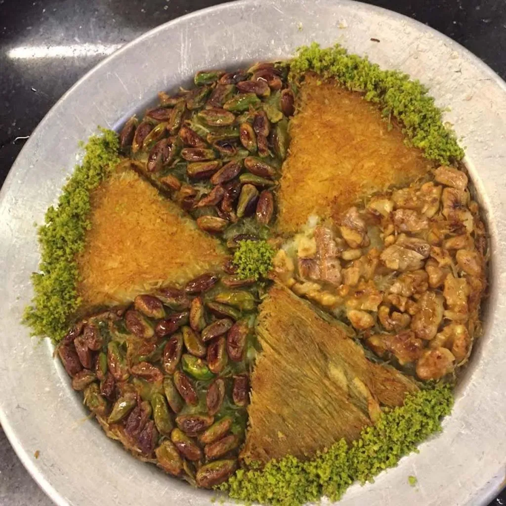 Round tray of künefe wedges at Keyfeder topped with whole pistachios, walnuts, and a rim of ground pistachio