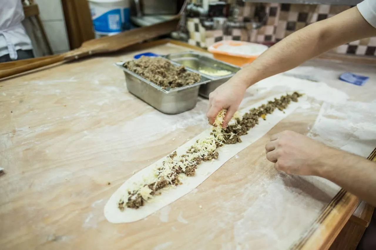 Long pide dough on a wooden bench being filled with cheese and ground meat