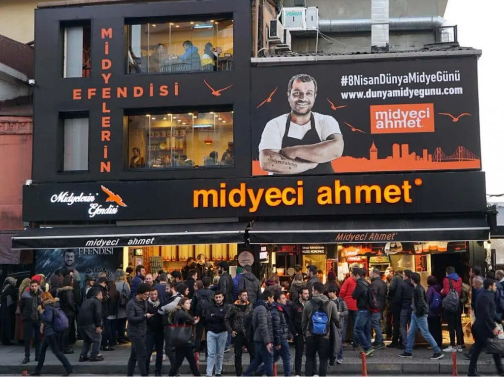 A crowd gathered outside the black and orange Midyeci Ahmet storefront in Beşiktaş