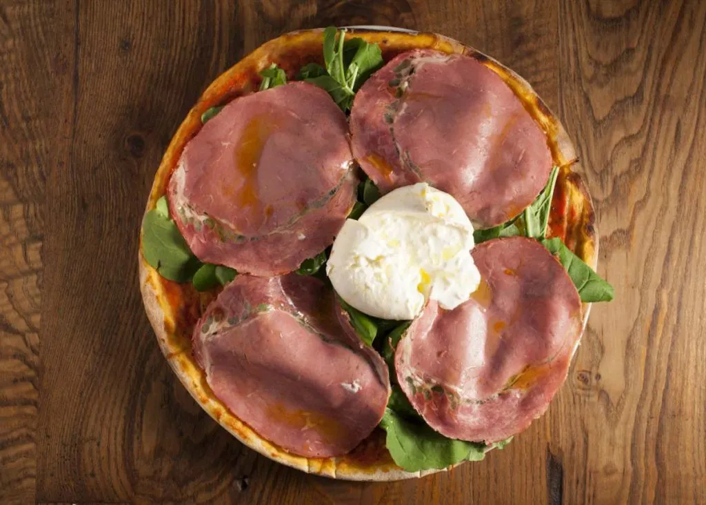 Overhead view of a Miss Pizza thin-crust pie topped with cured beef slices, arugula, and a center of soft white cheese