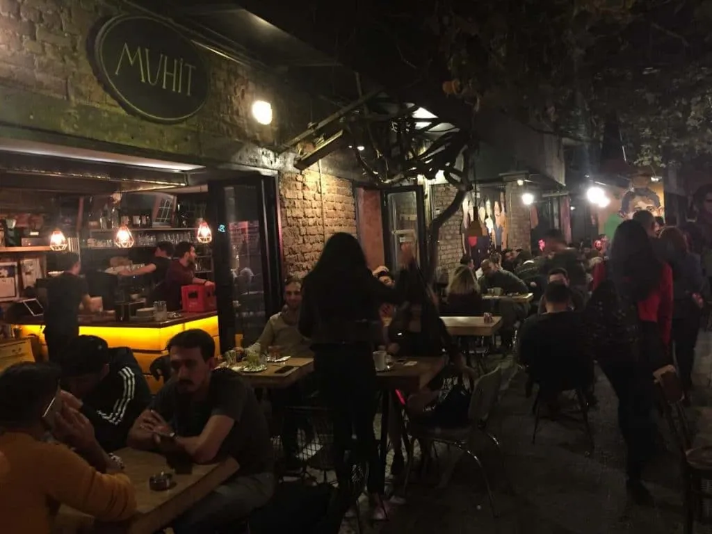 Evening crowd at Muhit's outdoor tables in a Karaköy alley, under the cafe's oval sign