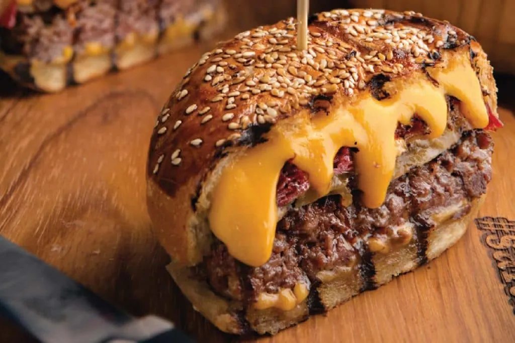 Nusr-et burger cut open on a wooden board, melted cheddar flowing over the beef inside a grill-marked sesame bun