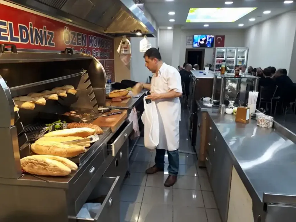 The grill line at Özen Kokoreç in Ortaköy, with loaves of bread warming over the fire and diners in the back