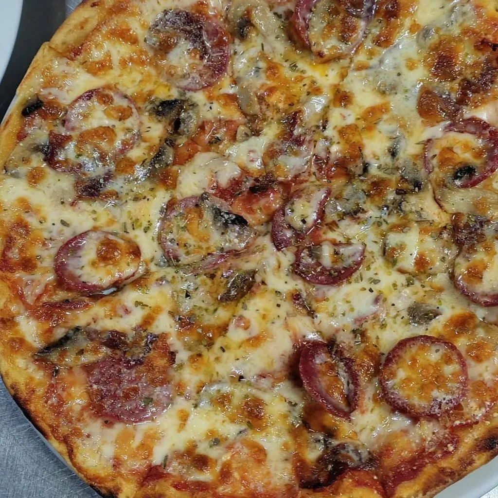 Close-up of a bubbling cheese pizza with cured sausage rounds and mushrooms at Ozi Pizza and Pasta