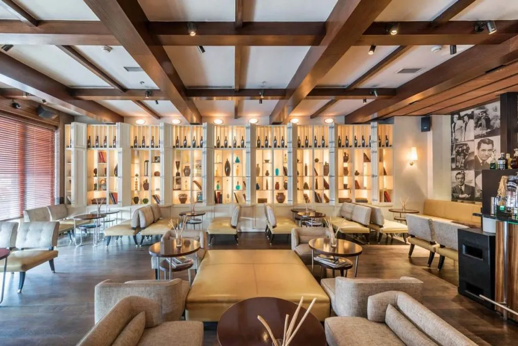 Paper Moon Istanbul's lounge with a coffered wood ceiling, backlit display shelves, leather seating, and black-and-white movie star portraits