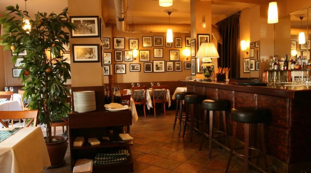 Pizzeria Pidos dining room with a dark wood bar, leather stools, and walls of framed black-and-white photographs
