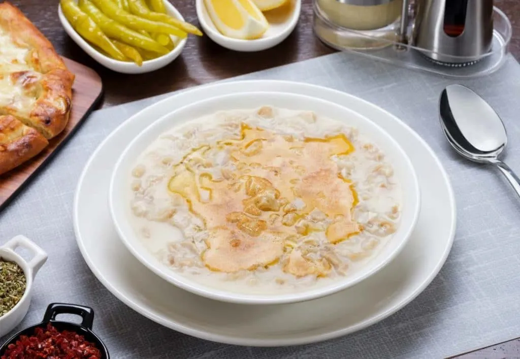 Creamy tripe soup topped with melted butter, served with lemon wedges, pickled peppers, and pide