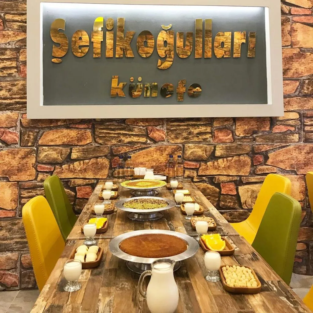 Long table at Şefikoğulları set with künefe trays, jugs and glasses of milk, orange slices, and nuts