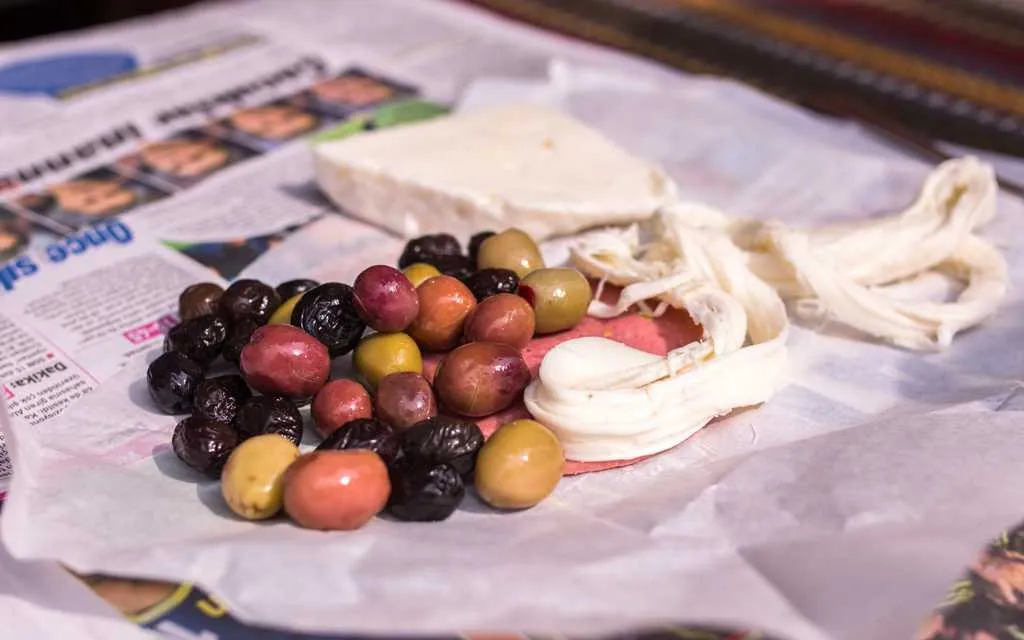 Mixed olives, string cheese, white cheese and cured meat laying on top of paper