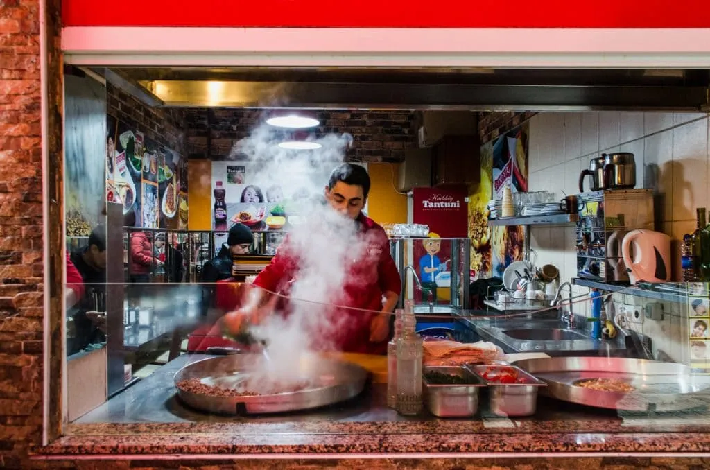 Chef cooking tantuni on a circular metal stove with steam rising through the kitchen