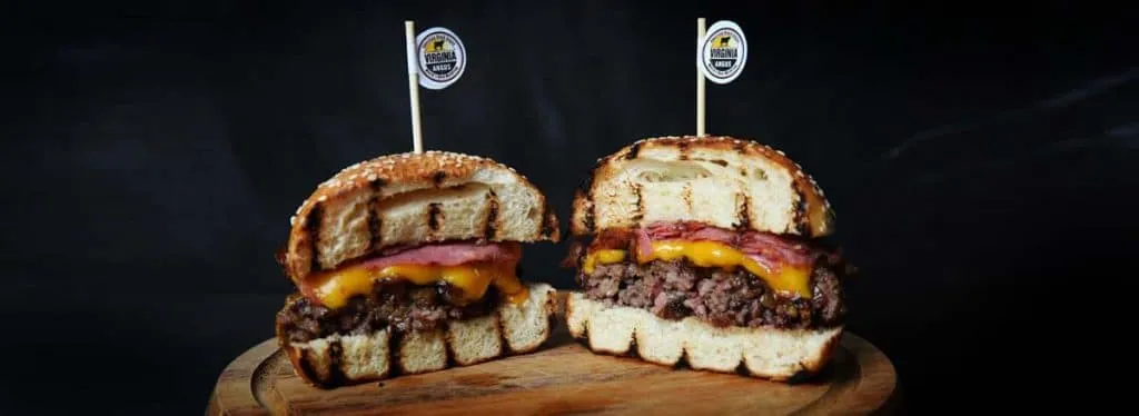 Halved Virginia Angus burger on a wooden board, grill-marked sesame bun with melted cheddar and branded picks